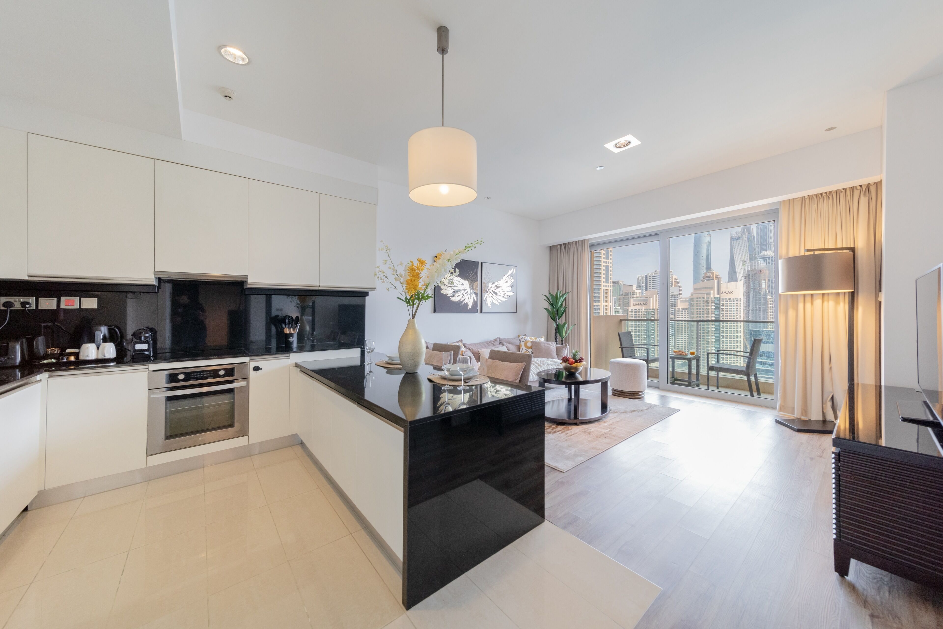 A modern kitchen with a central island, a dining area with a round table, and a large window offering a city view.