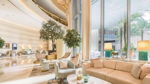 Un hall d’entrée spacieux, doté d’un haut plafond, de grandes fenêtres et d’un espace salon central avec un canapé et des fauteuils.