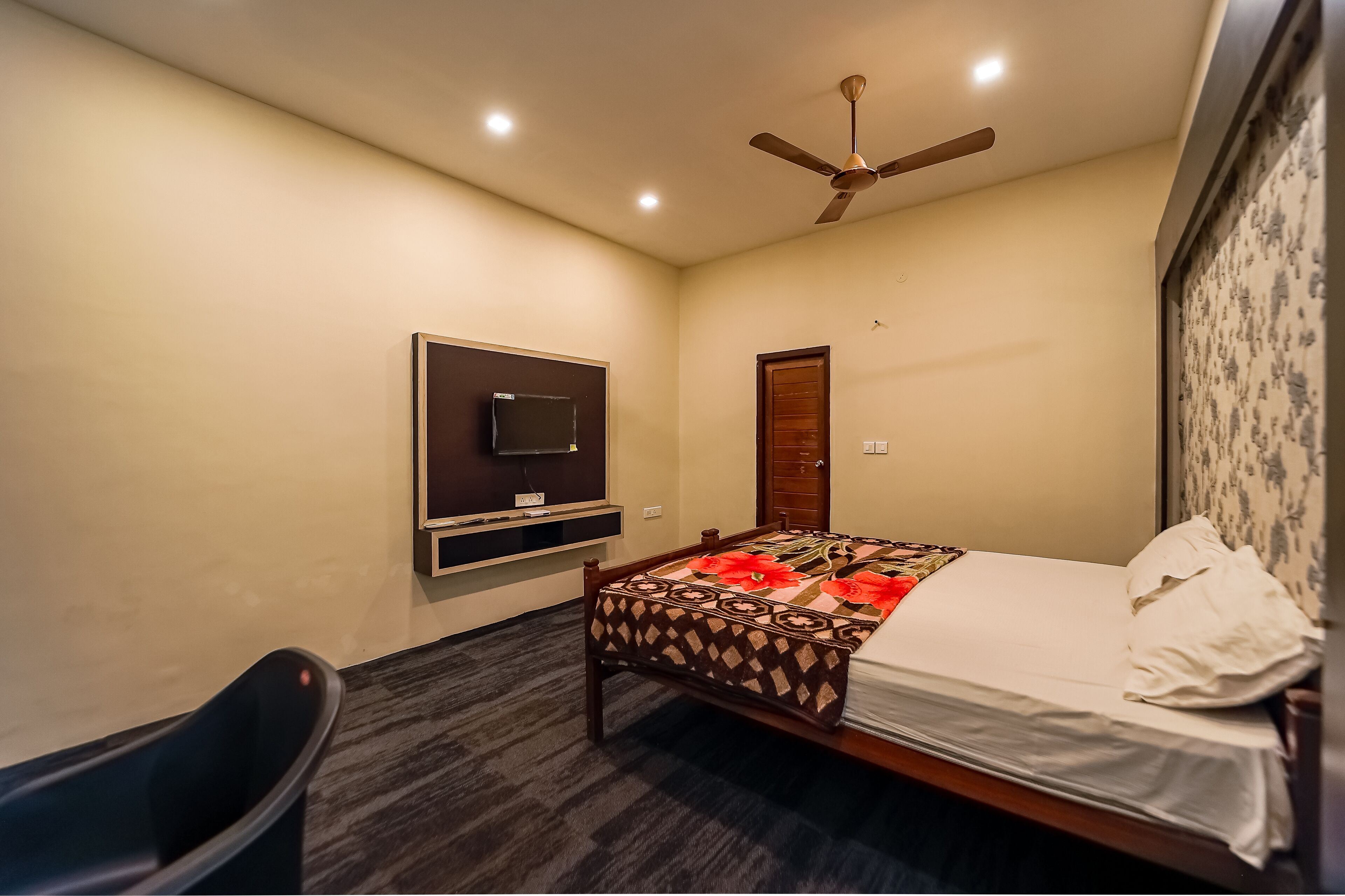 Une chambre d’hôtel avec un lit, un téléviseur fixé au mur, un ventilateur de plafond et une porte.