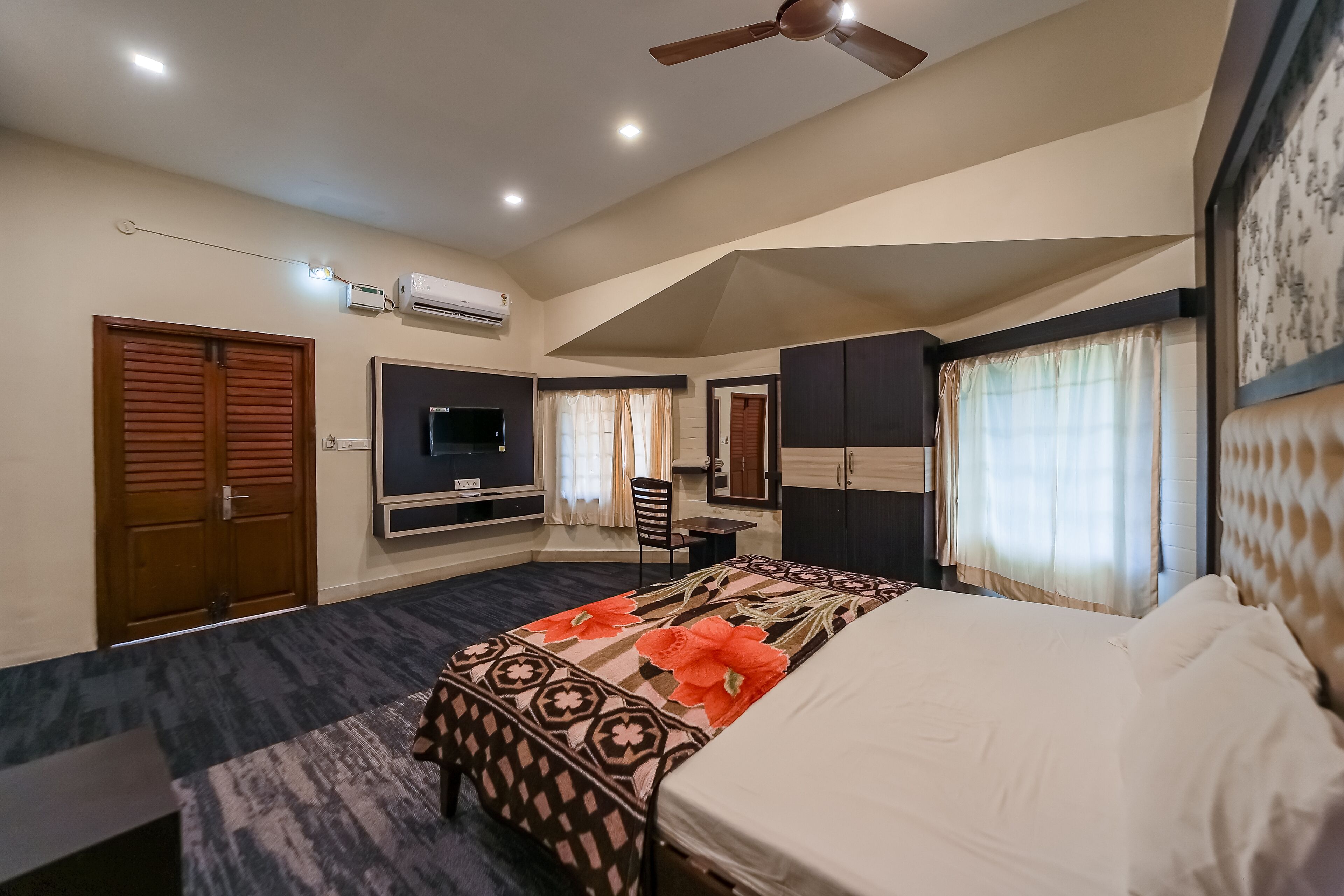 A hotel room with a bed, a desk, a chair, a TV, and a ceiling fan.