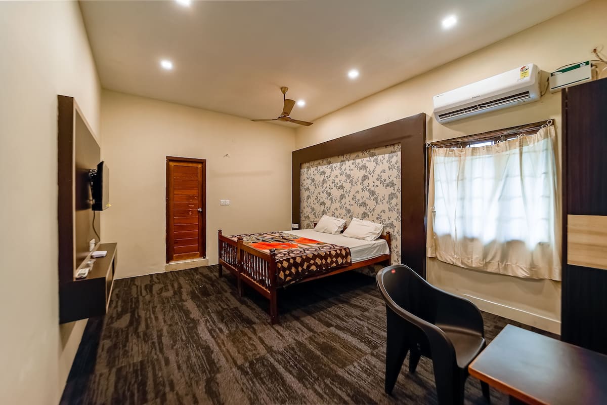 A hotel room with a bed, a desk, a chair, an air conditioner, a ceiling fan, and a door.