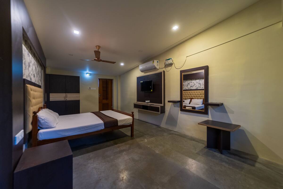 A modern hotel room with a single bed, a small table, a TV mounted on the wall, and a ceiling fan.