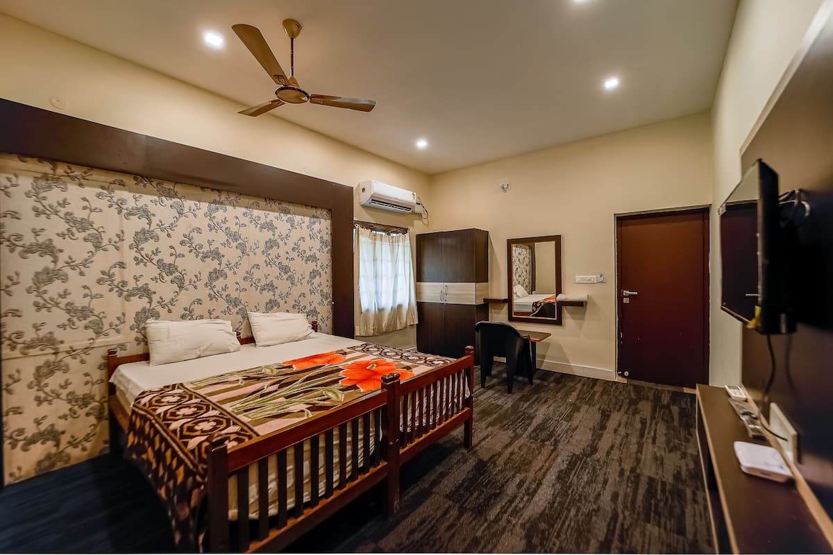 A hotel room with a bed, a desk, a chair, a ceiling fan, an air conditioning unit, a television, and a wardrobe.