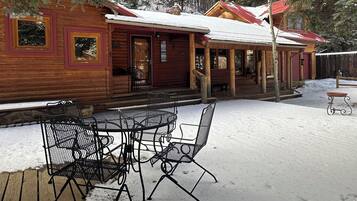 A wooden cabin with a porch, a table and chairs, and a snow-covered ground.