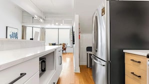 Une cuisine moderne avec des meubles blancs, un réfrigérateur en acier inoxydable et un plancher en bois.