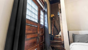 Une chambre avec une porte en bois, un lit avec une literie grise et un escalier menant à un étage supérieur.