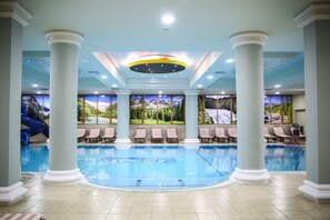 Una amplia piscina cubierta con columnas blancas, un tobogán azul y murales decorativos en las paredes.