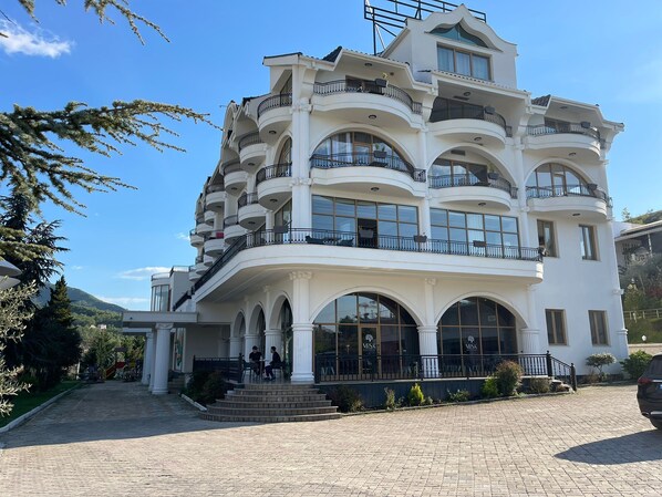 Un edificio de varios pisos con balcones, ventanas amplias y un área de entrada empavedada.