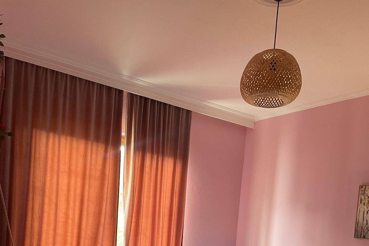 A bedroom with a bed, curtains, a hanging light fixture, and a painting on the wall.