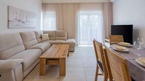 Un salon moderne avec un canapé, une table basse en bois et un coin repas avec une table dressée pour deux personnes.