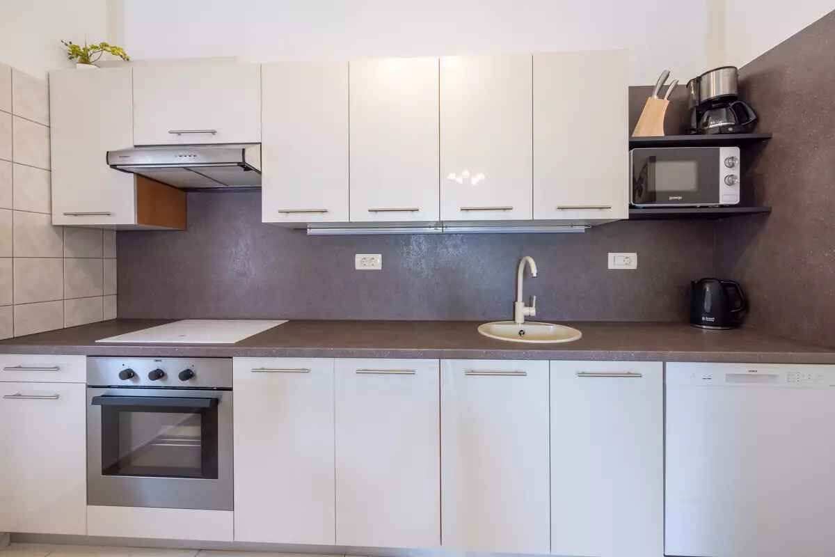 Una cocina moderna con armarios blancos, horno empotrado, microondas y cafetera sobre la encimera.