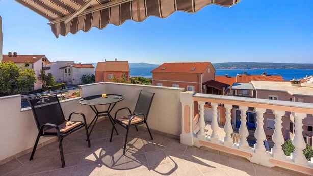 Un balcon avec une table et des chaises, offrant une vue sur la côte, avec des bâtiments et la mer.