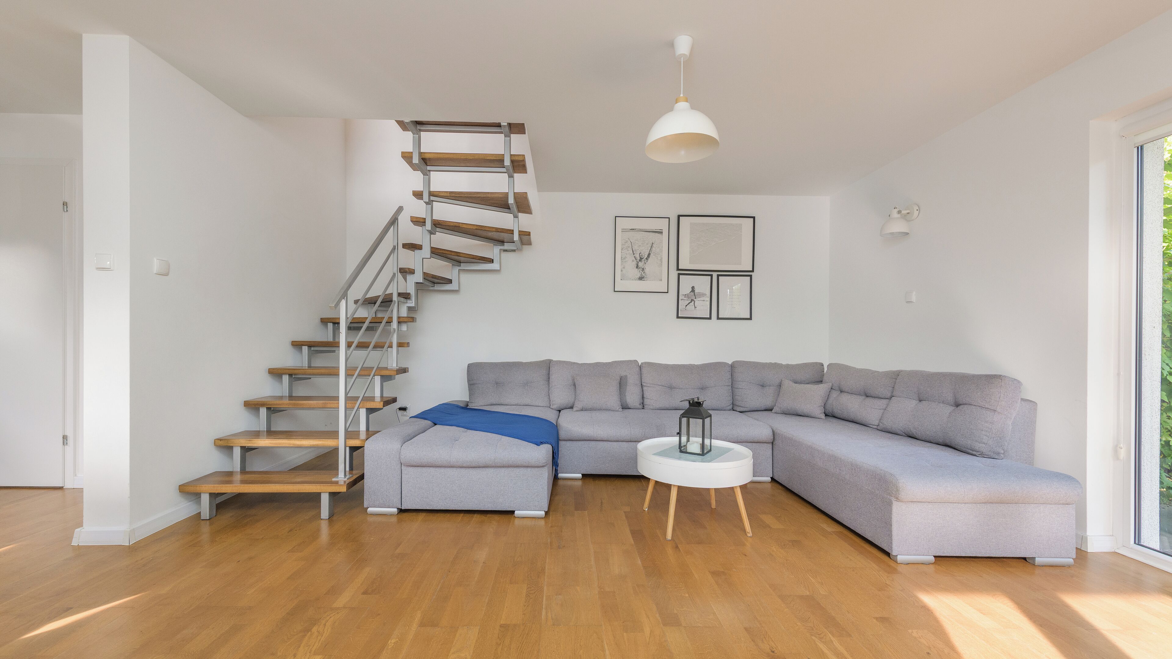 A modern living room with a wooden staircase, a grey sectional sofa, and a round side table.