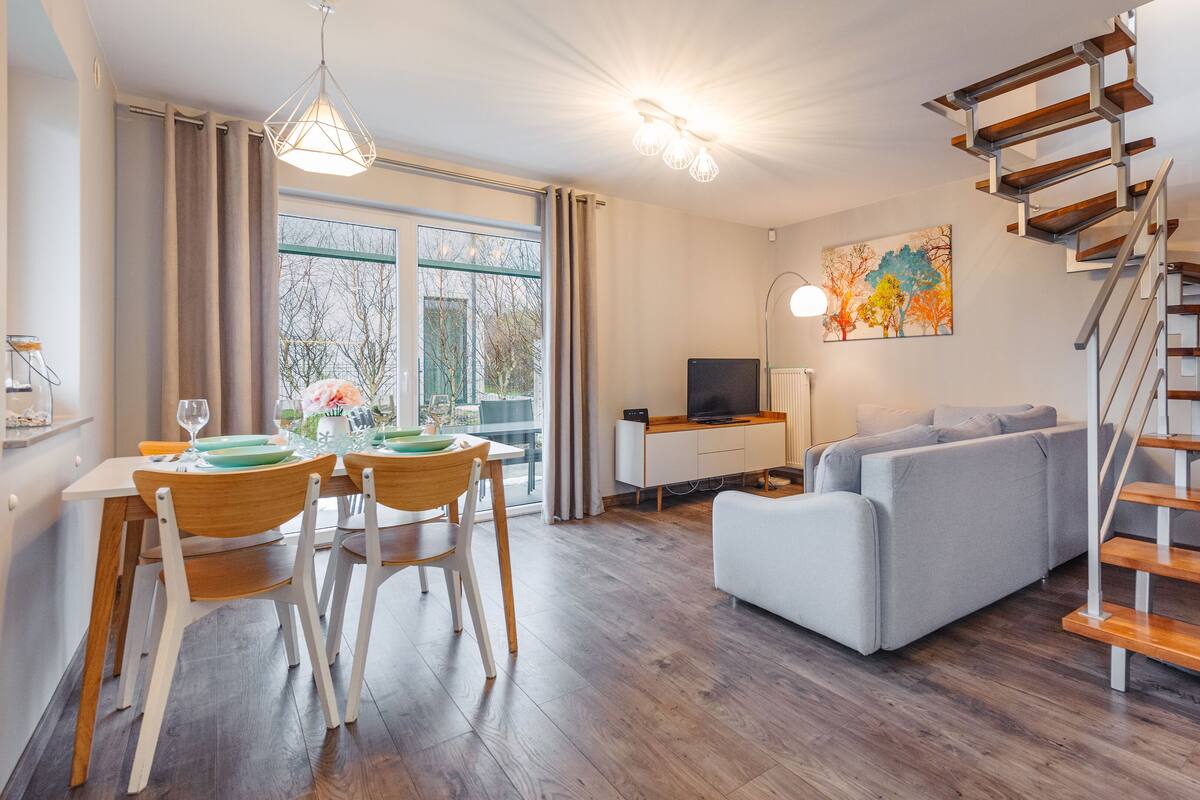 Ein modernes Wohnzimmer mit Treppe, Essbereich und Fernseher auf einem Holzkabinett.