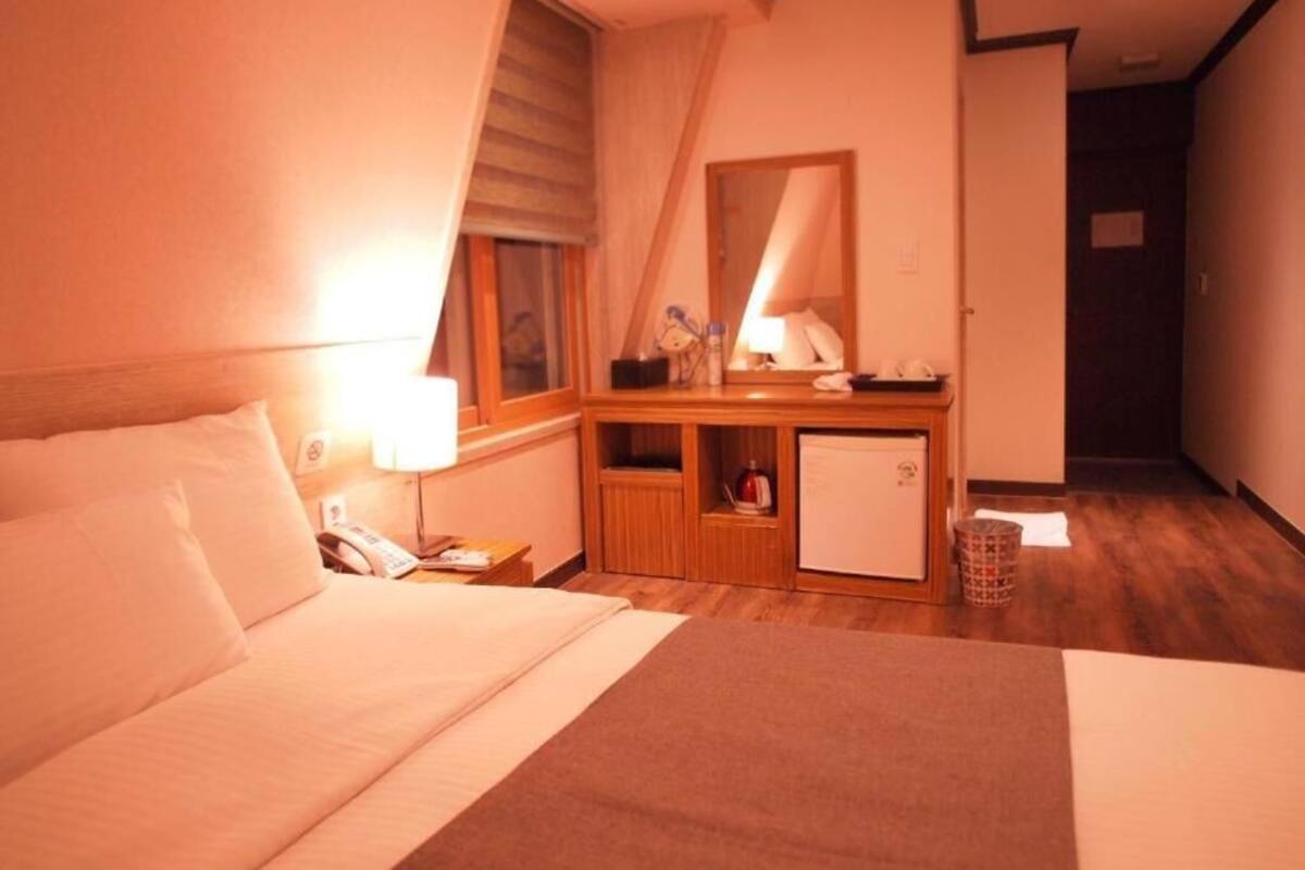 A hotel room with a bed, bedside table, lamp, and a small kitchenette area.