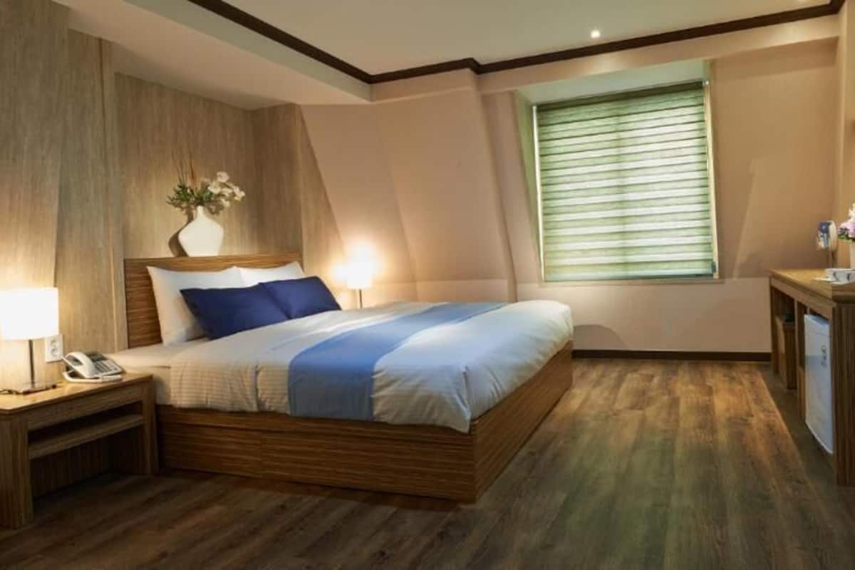 A modern hotel room with a wooden bed, bedside tables, a desk, and a TV.