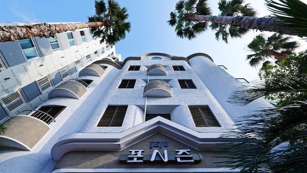 A modern hotel with a unique architectural design, featuring multiple balconies and a prominent entrance sign. - Fourseasons Hotel (Jeju City)