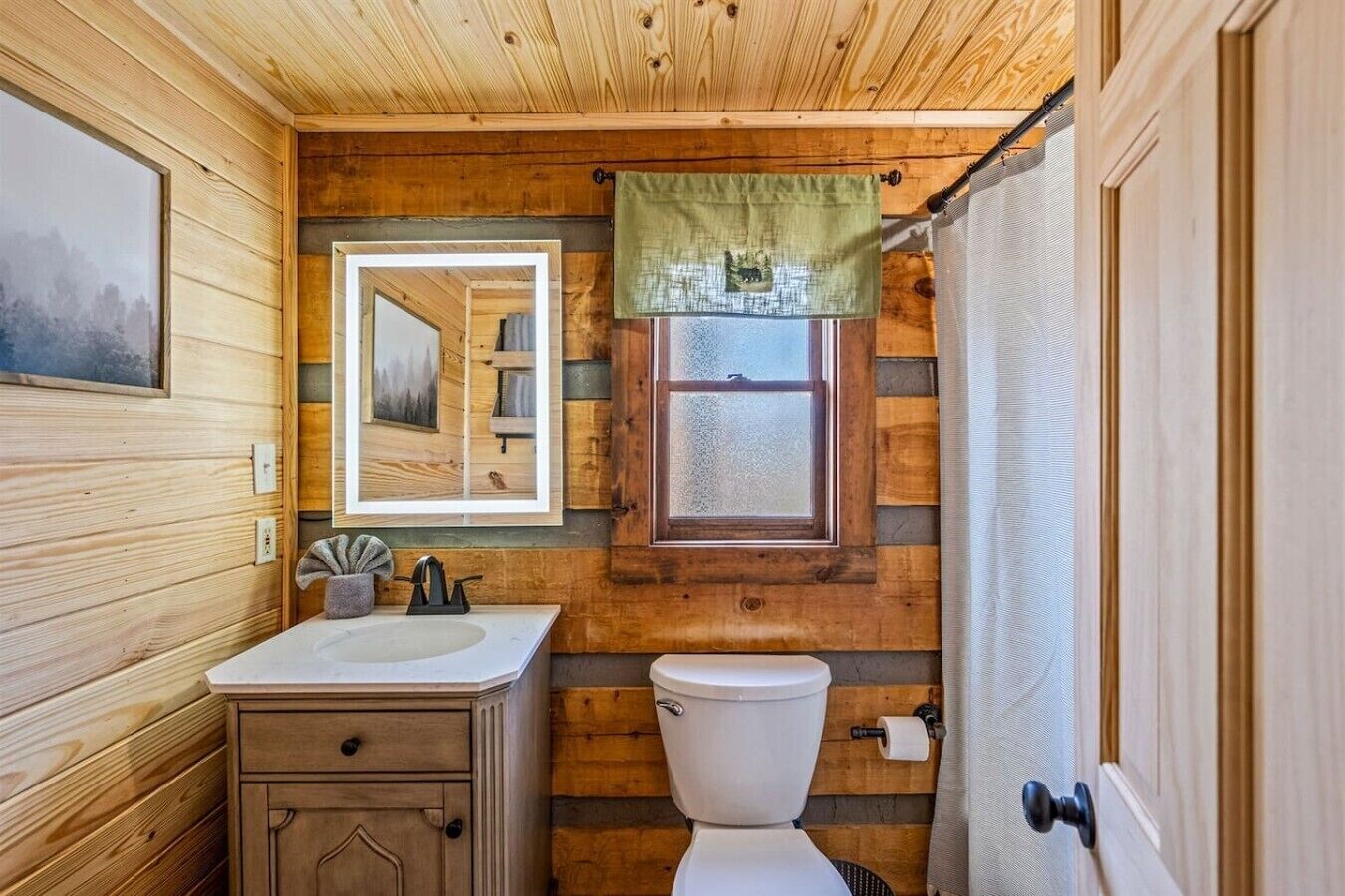 A wooden cabin bathroom with a sink, toilet, and a window.