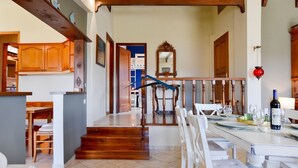 Un comedor amplio con una mesa larga dispuesta para una comida, una escalera que sube a otro nivel, y detalles arquitectónicos de madera.