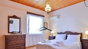 Un dormitorio con techo de madera, una cama grande con ropa de cama blanca, un aparador, un espejo y una ventana con cortinas.