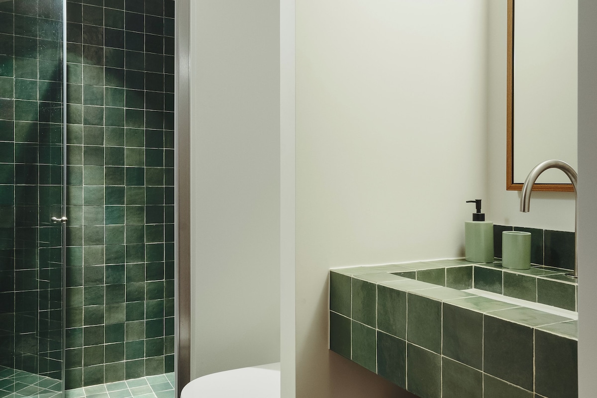 Un baño con inodoro, lavabo, espejo y zona de ducha.