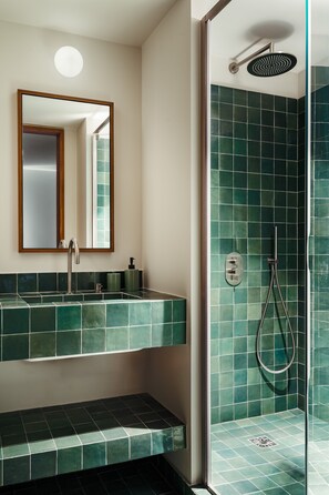 Un baño con ducha de azulejos verdes, un lavabo con espejo y un banco.