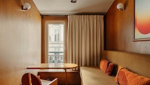 Ett hotellrum med en väggpanel av trä, en soffa med orange kuddar, ett litet skrivbord i trä och ett fönster med gardiner.