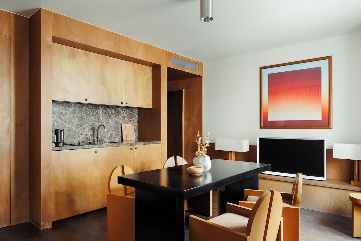 A modern kitchen with wooden cabinets, a marble countertop, and a black dining table with chairs.