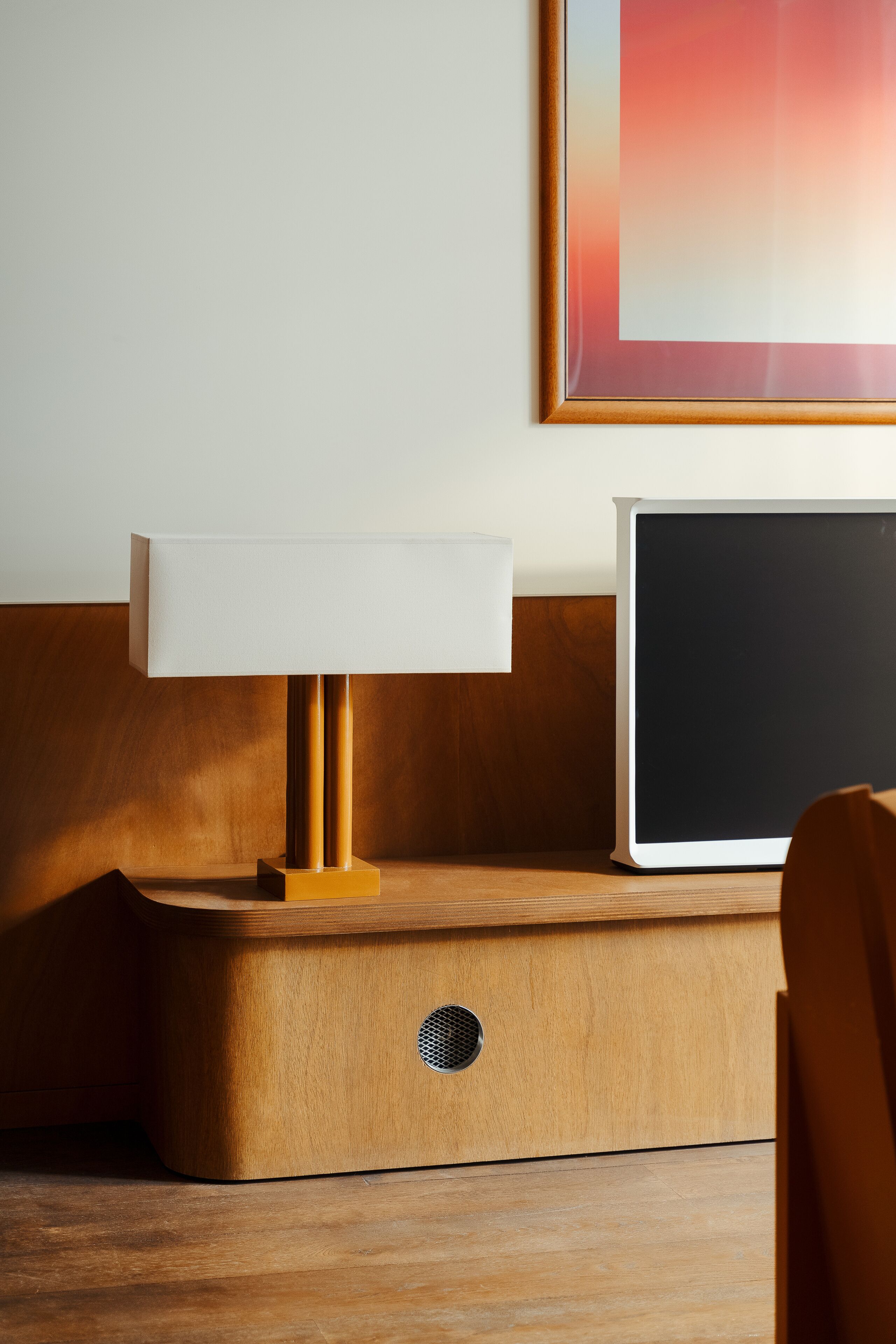 A wooden bedside table with a lamp and a laptop.