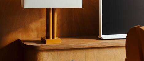 A wooden bedside table with a lamp and a laptop.