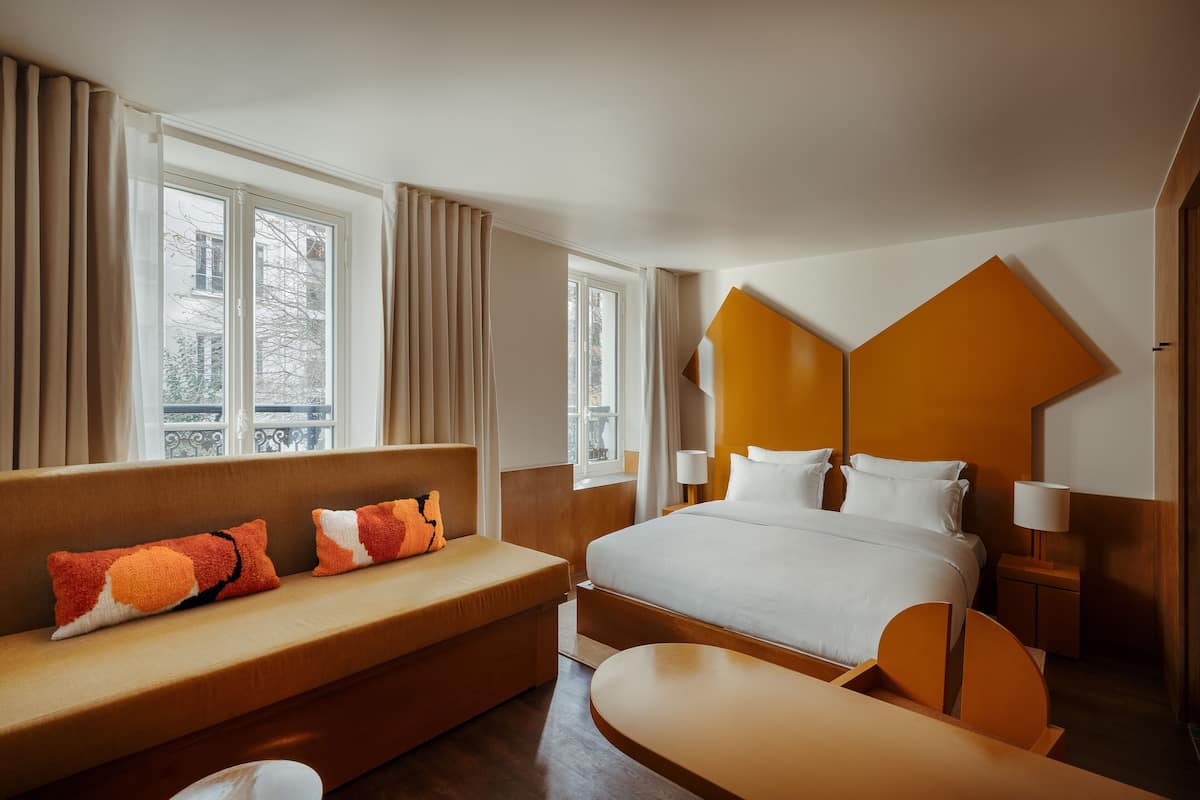 A hotel room with a large bed, a sofa, a desk, and a window with curtains.