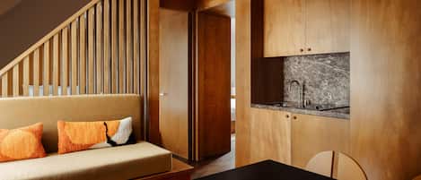 Un interior moderno con una escalera de madera, un sofá con cojines naranja, una zona de cocina con encimera de mármol y una mesa de comedor.