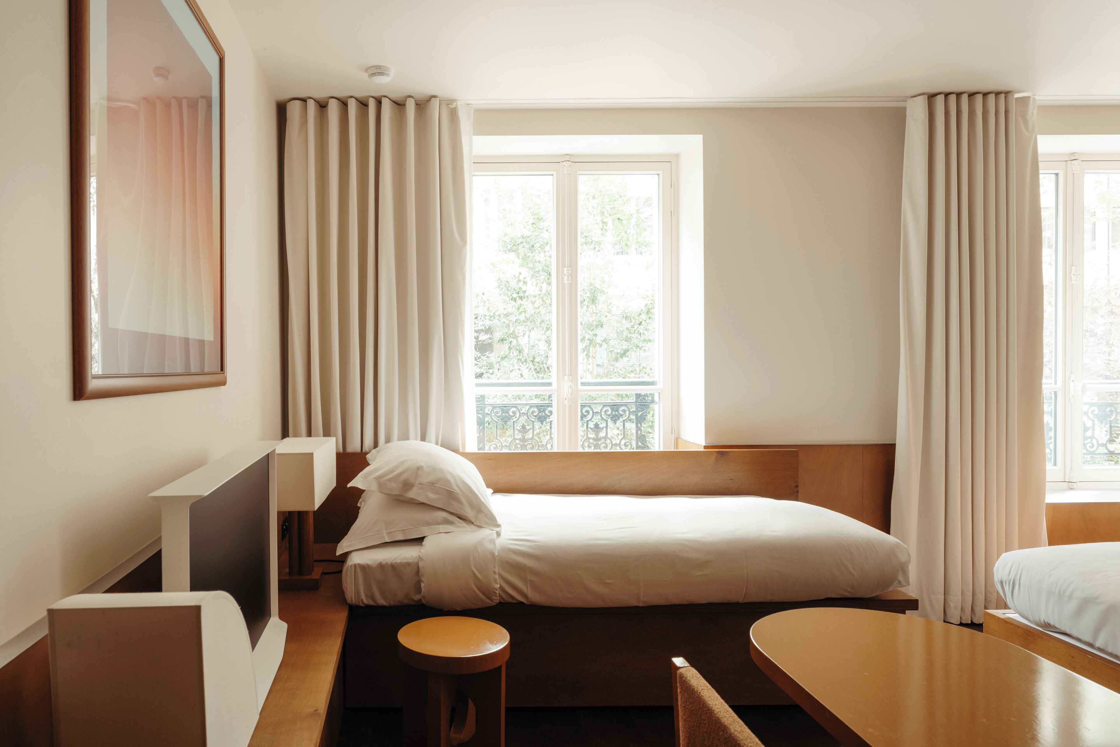 Ett hotellrum med en säng, ett skrivbord, en stol, ett fönster med gardiner och utsikt över grönområden utanför.