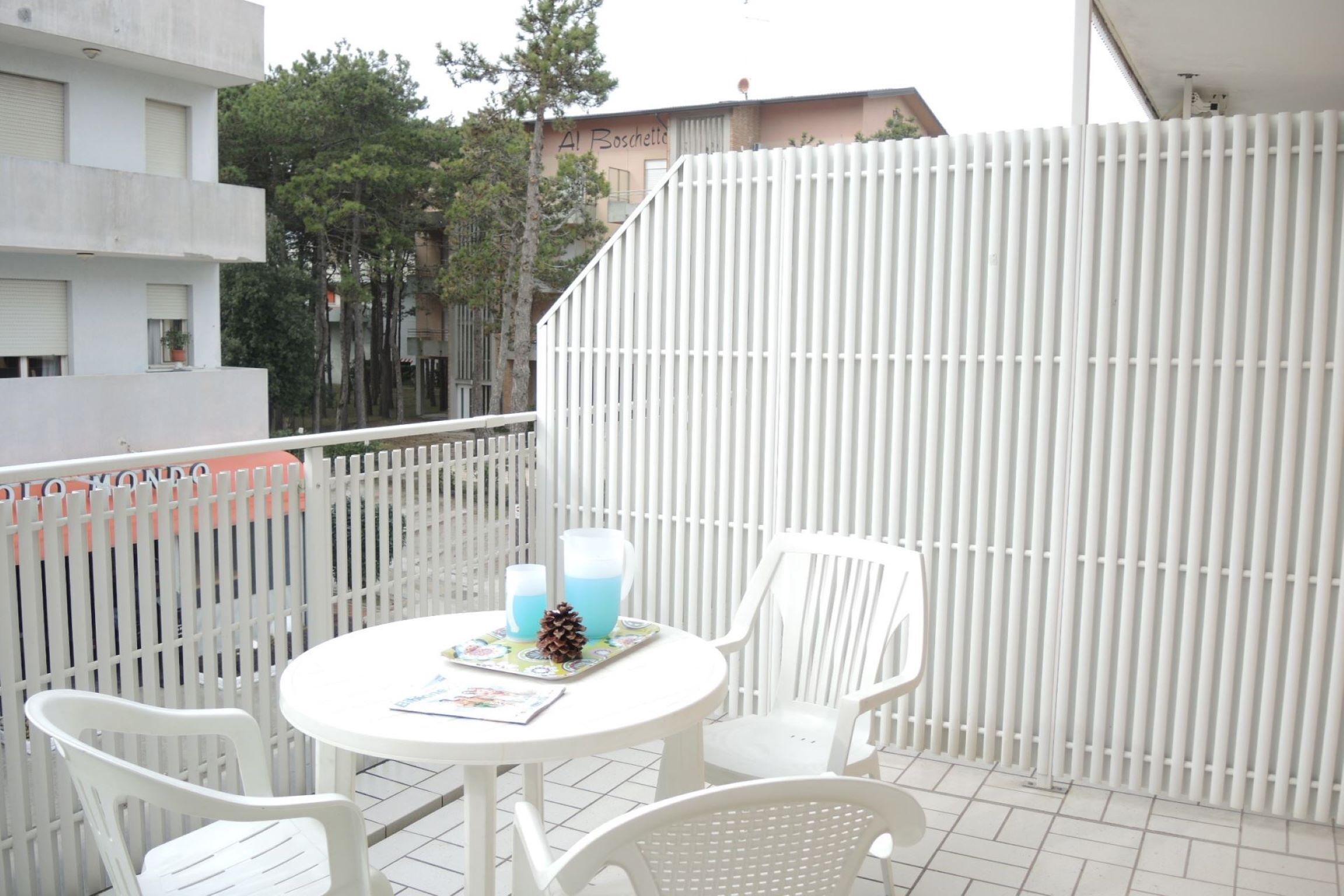 A balcony with a white table and chairs, a white fence, and a building in the background.
