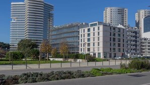 A modern urban area with high-rise buildings, a clear sky, and a well-maintained road with minimal traffic.