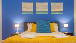 A hotel room with a bed, two bedside tables, and three wall-mounted paintings.