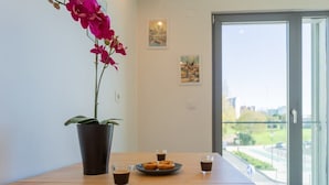 A table with a potted orchid, a plate of donuts, and four glasses of coffee in a room with a glass door and a view of a cityscape.