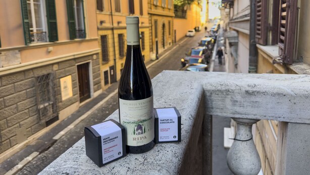 Uma garrafa de vinho e duas caixas de lanches em um corrimão de varanda com vista para a rua.
