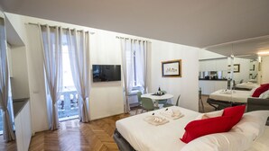 Quarto de hotel com cama, escrivaninha, cadeira, mesa pequena com uma garrafa e televisão.