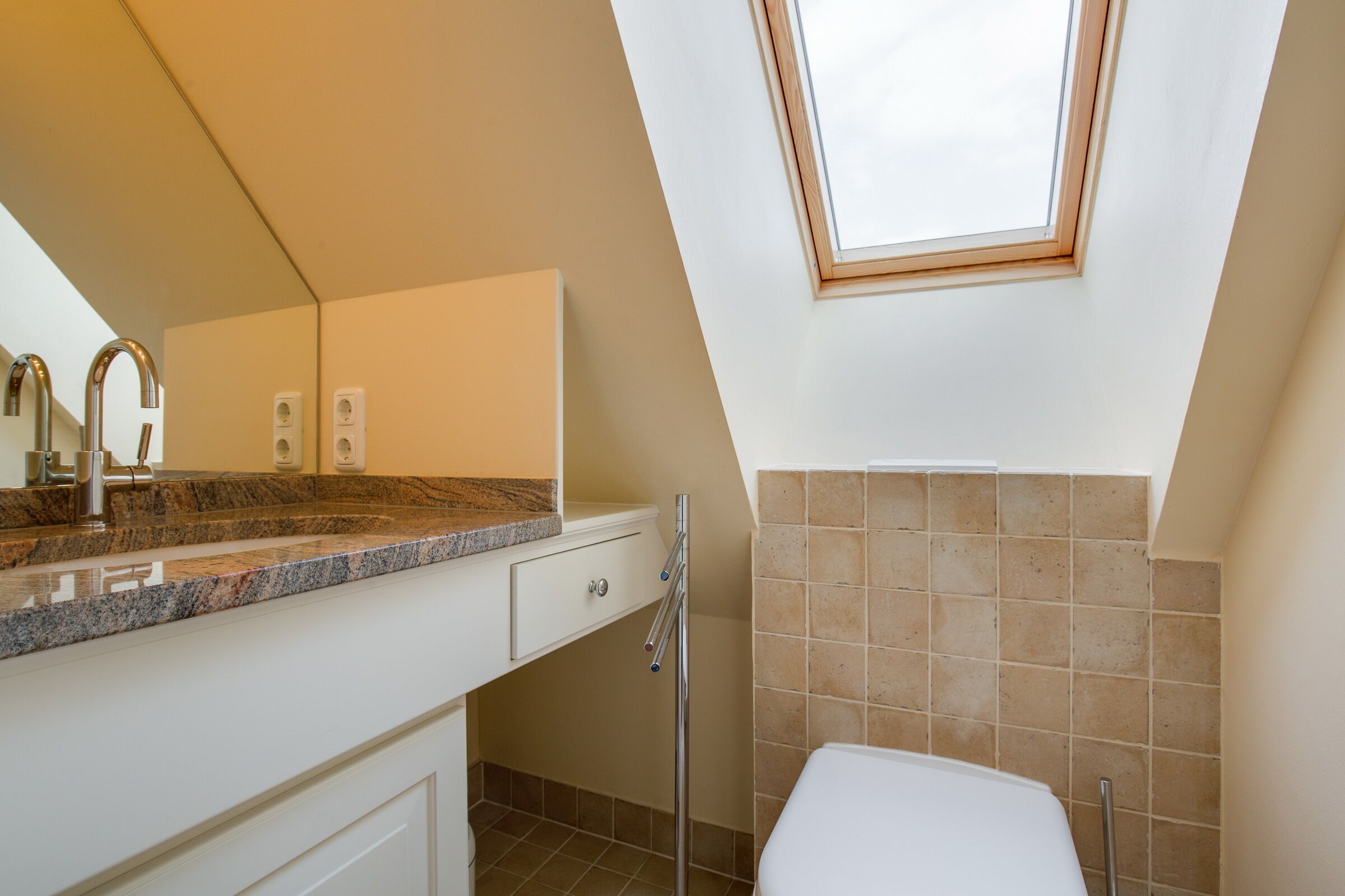Une salle de bain dotée d’un puits de lumière, d’un lavabo avec un plan de travail en granit et de toilettes.