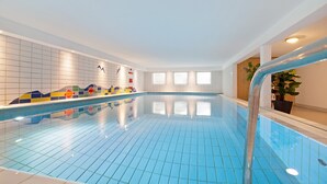 Una piscina interior con azulejos azules, una pared revestida de azulejos con diseños coloridos y una planta en maceta.