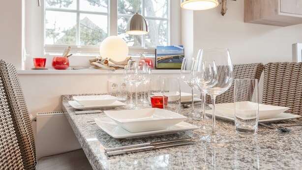 Una cocina con una mesa de comedor preparada para cuatro personas, equipada con platos blancos, vasos y cubiertos.