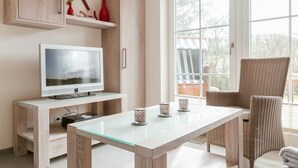 Una sala moderna con una mesa de comedor de vidrio, un televisor de pantalla plana, mobiliario de mimbre y un ventanal que ofrece vistas al exterior.