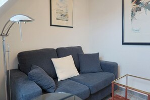 Una sala de estar moderna con un sofá gris, una almohada blanca, una mesa de centro de vidrio y una lámpara de pie.