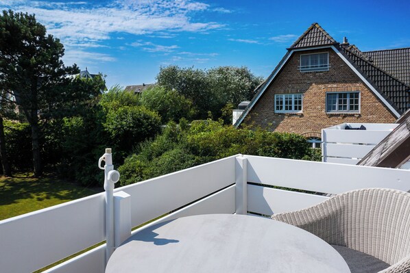 A balcony with a white railing, a round table, and a wicker chair.