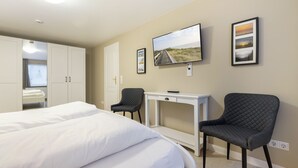 Ett hotellrum med två sängar, ett skrivbord, en stol, en tv och inramade tavlor på väggen.