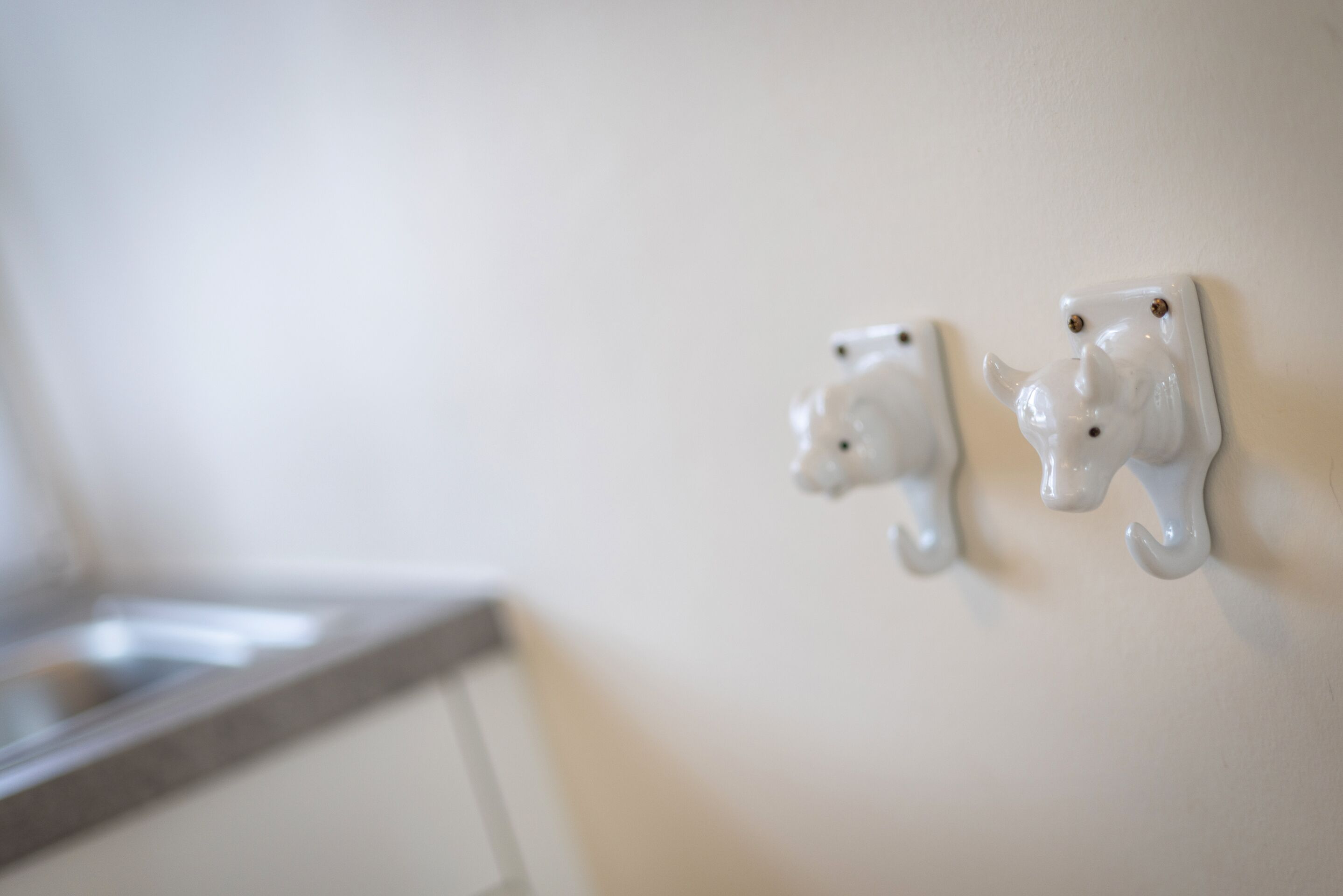 Deux crochets muraux en céramique blanche, fixés sur un mur blanc.