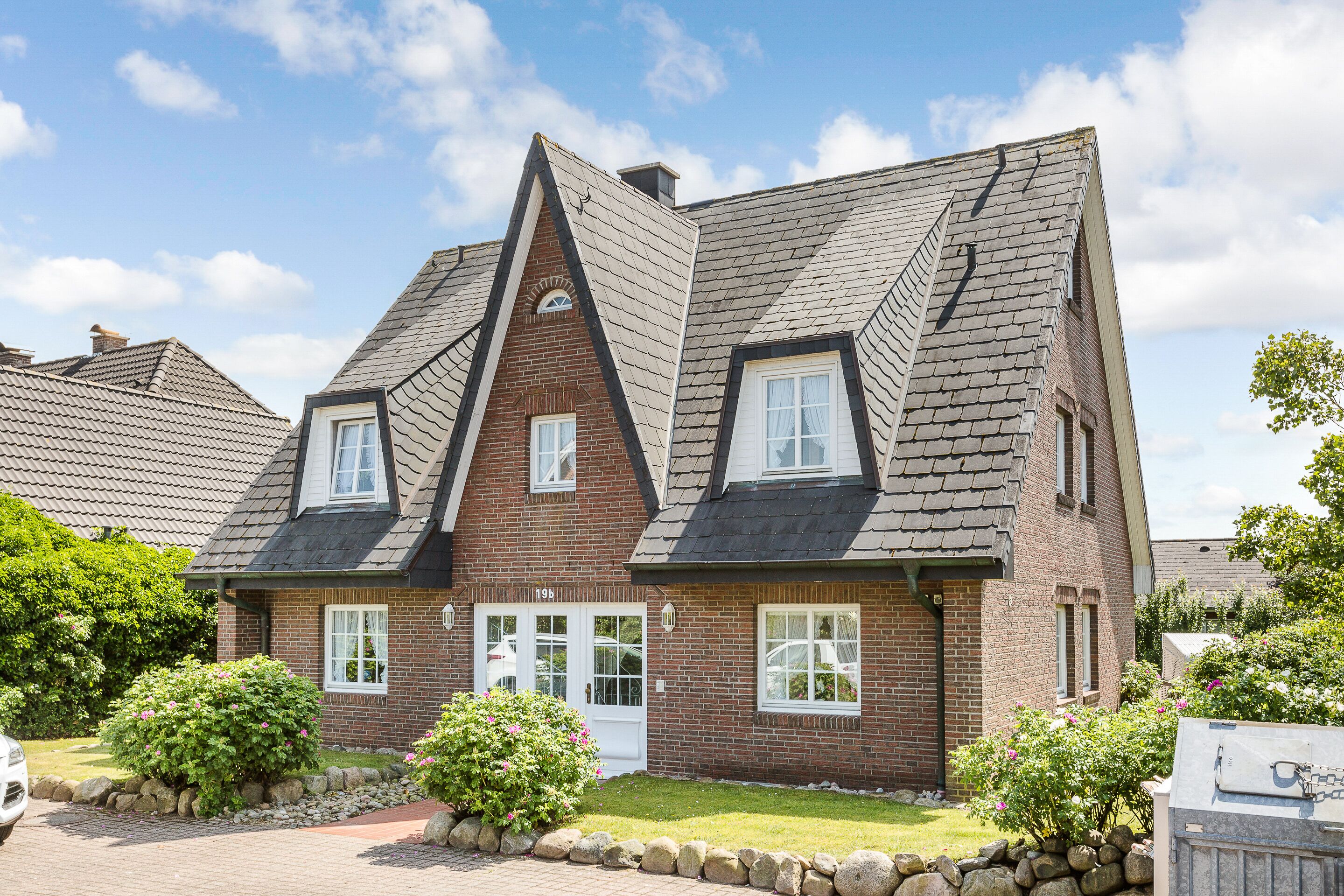 A two-story brick house with a steeply pitched roof, dormer windows, and a stone pathway leading to the entrance.