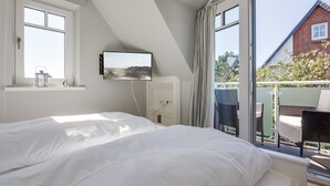 A bedroom with a large bed, a TV mounted on the wall, and a balcony with wicker chairs. - Ein Wohntraum & Viel Mehr, Nahe dem Meer (Sylt / OT Westerland)