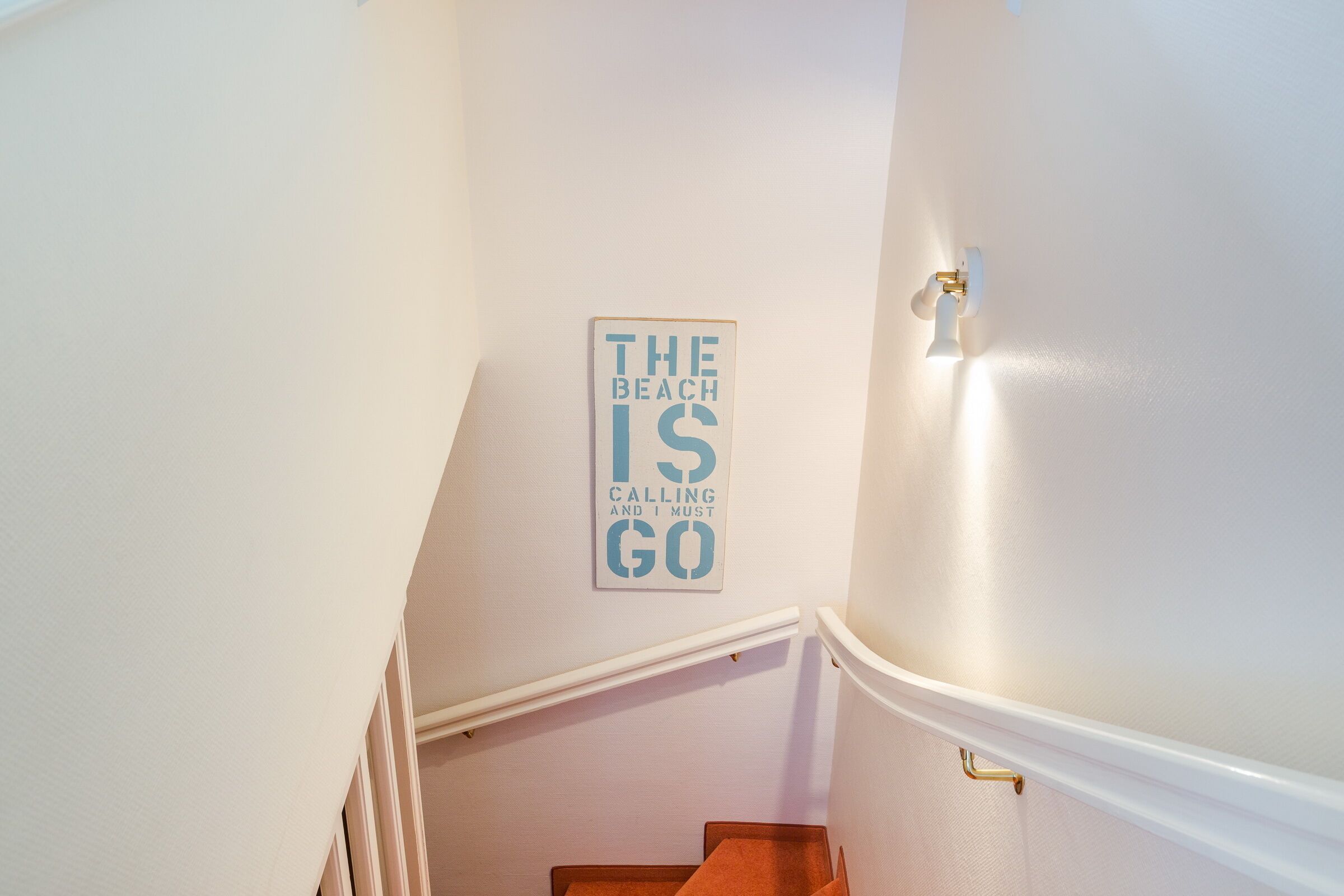 A staircase with a sign on the wall that reads "THE BEACH IS CALLING AND I MUST GO".